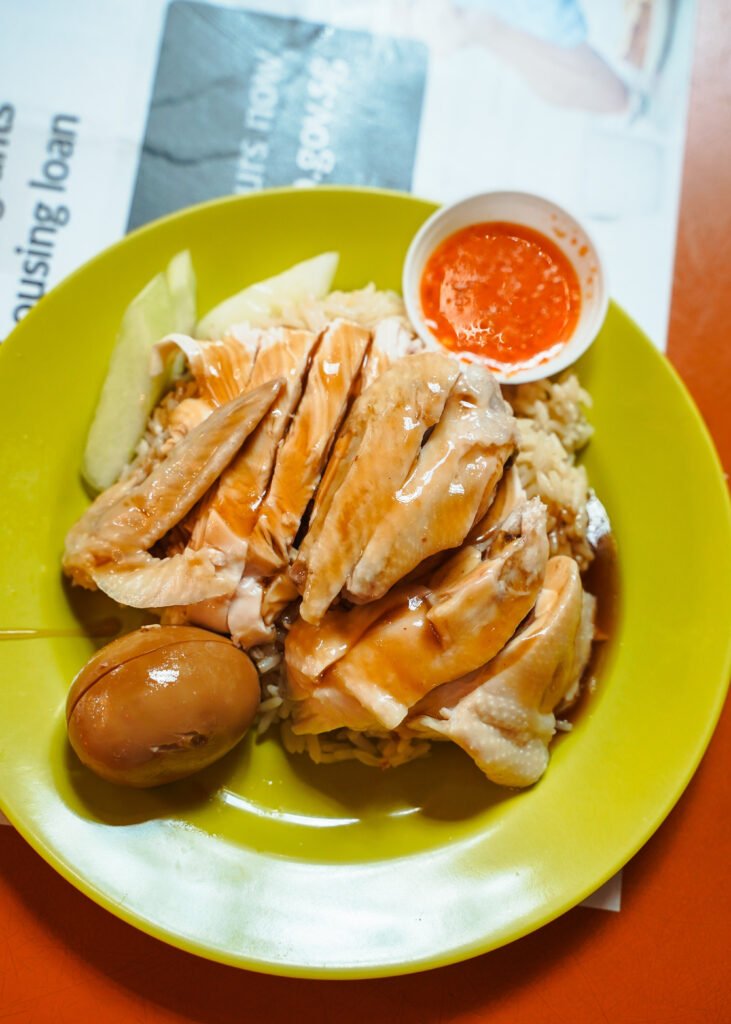 Plate of hainan chicken rice with glistening gravy and an egg and condiments